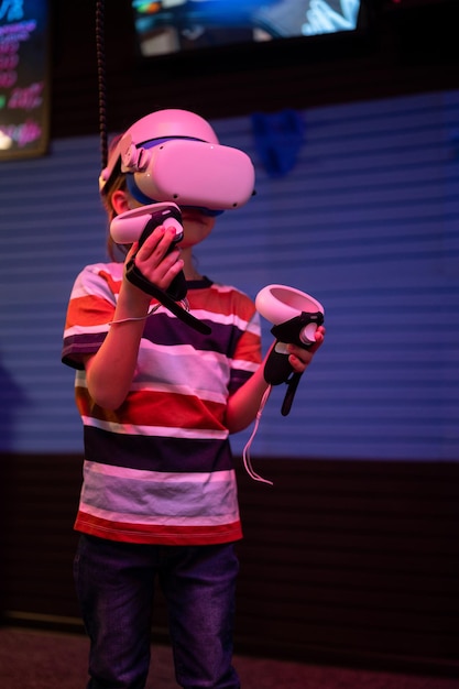 Vr game and virtual reality kid boy gamer six years old fun
playing on futuristic simulation video game in 3d glasses and
joysticks in entertainment vr room with innovation technology and
neon light