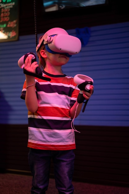 Foto gioco vr e realtà virtuale kid boy gamer divertimento di sei anni giocando su un videogioco di simulazione futuristica in occhiali 3d e joystick nella sala vr di intrattenimento con tecnologia innovativa e luce al neon