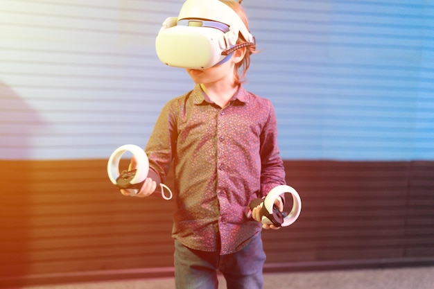 Виртуальная игра и виртуальная реальность, шестилетний мальчик-геймер, весело играющий в футуристический симулятор видеосъемки или исследующий учебную игру в 3D-очках и джойстиках в виртуальной комнате с технологической вспышкой