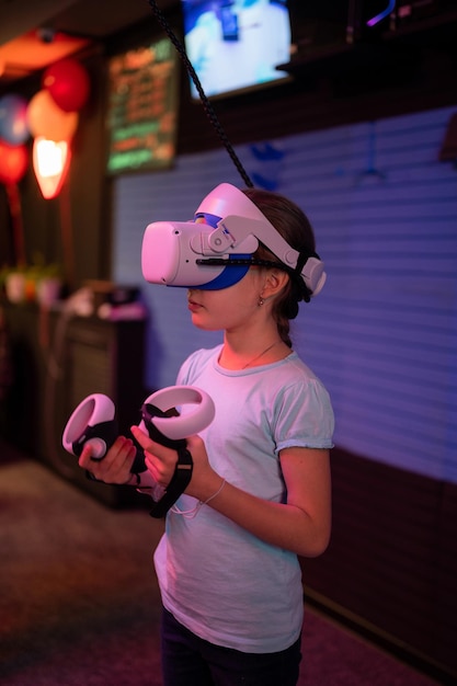 Vr game and virtual reality kid girl gamer eight years old fun
playing on futuristic simulation video game in 3d glasses and
joysticks in entertainment vr room innovation technology and neon
light