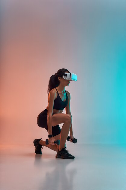 Vr technology side view of young sporty woman in sports clothing exercising with dumbbells while