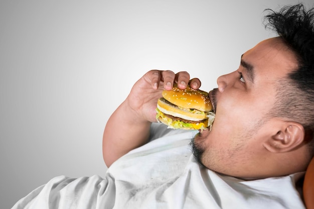 Vraatzuchtige dikke man die een hamburger eet op studio