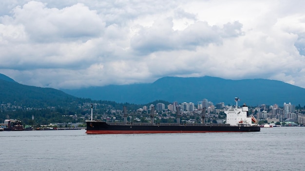 Vrachtschip boot zeeschip scheepvaart transport drijvend langs de zeekust en de skyline van Vancouver