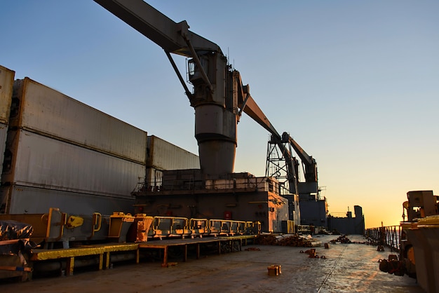 Vrachtschip dek met kranen en containers bij zonsondergang