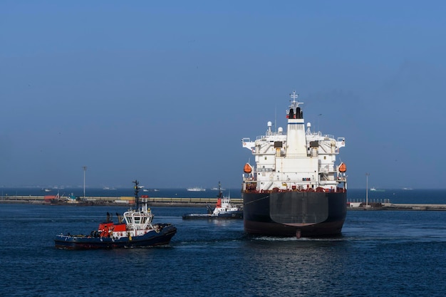 Vrachtschip gaat naar zee vanuit de haven met sleepbootassistentie Bulkcarrier Droog vrachtschip