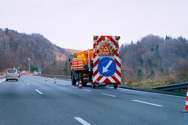 Vrachtwagen met pijl naar beneden links reflecterende richting verkeersbord in snelweg. Signaal voor wegwerkzaamheden. Verkeersindicator voor smalle rijstroken.