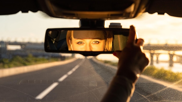 Vreedige vrolijke vrouw die de spiegel aanpast terwijl ze in haar auto zit en naar de reflectie in de camera kijkt