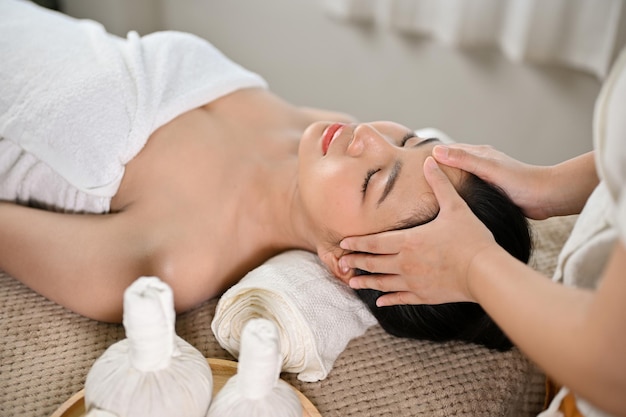 Vreedzame Aziatische vrouw liggend op massagebed met gezichtsbehandeling door een professionele masseur