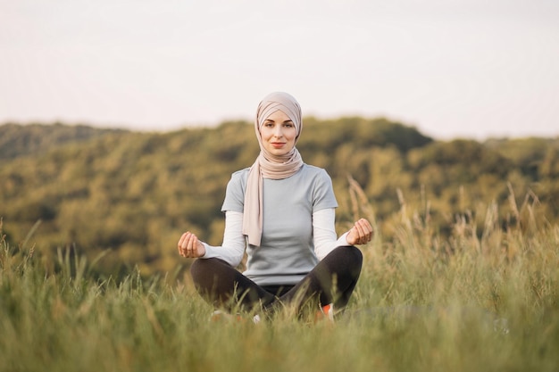 Vreedzame jonge dame in hijab die mediteert terwijl ze naar de camera in het park kijkt
