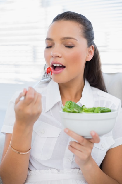 Vreedzame mooie vrouw die gezonde saladezitting op bank eet