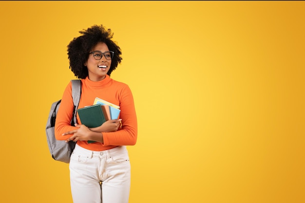 Vreemde Afrikaans-Amerikaanse jonge dame met een bril en krullend haar die kleurrijke boeken vasthoudt