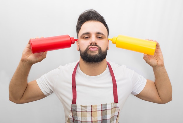 Vreemde man staan en poseren. Hij houdt twee kleurrijke flessen vast. Rode met ketchup en gele met mosterd. Hij steekt zijn lippen uit en houdt de ogen een beetje gesloten.