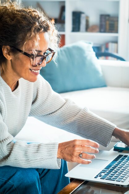 Vreemde oudere volwassen freelance zakenvrouw met een bril die thuis werkt met een laptop die op de bank rusten, op de computer typen, lachen, wegkijken Senior dame online winkelen