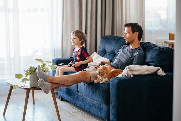 Vreemde vader en zoon spelen thuis videospelletjes op de bank met een roze kat.