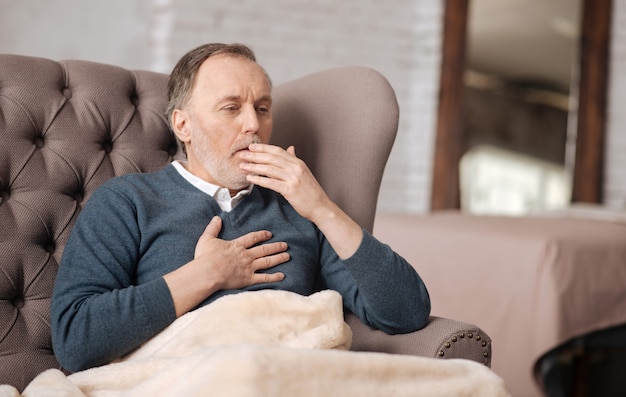 Vreselijke bronchitis. Senior knappe man hoest echt sterk terwijl hij thuis op de bank zit en.