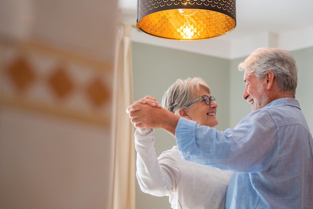 Vreugdevol actief oud gepensioneerd romantisch stel dat danst en lacht in de woonkamer gelukkige vrouw van middelbare leeftijd en oudere man die thuis plezier hebben glimlachende oudere familie grootouders ontspannen zich en binden samen xA