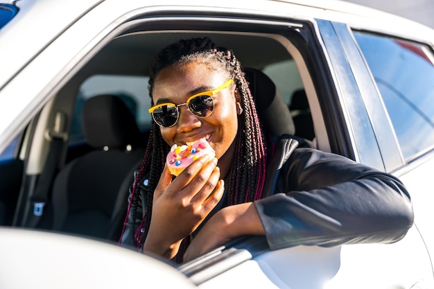 Vreugdevol Afrikaans meisje dat donuts eet leunt in het raam van de auto