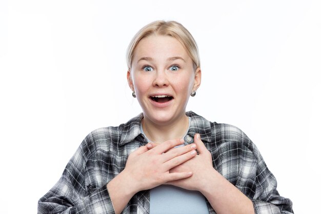 Vreugdevol tienermeisje een mooie blonde met sproeten op haar gezicht in een geruite shirt drukt emotioneel haar handen tegen haar borst een aangename onverwachte verrassing witte achtergrond closeup