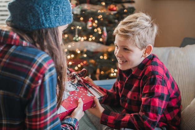 Vreugdevol vrouw geschenk aan zoon thuis tijdens kerstmis