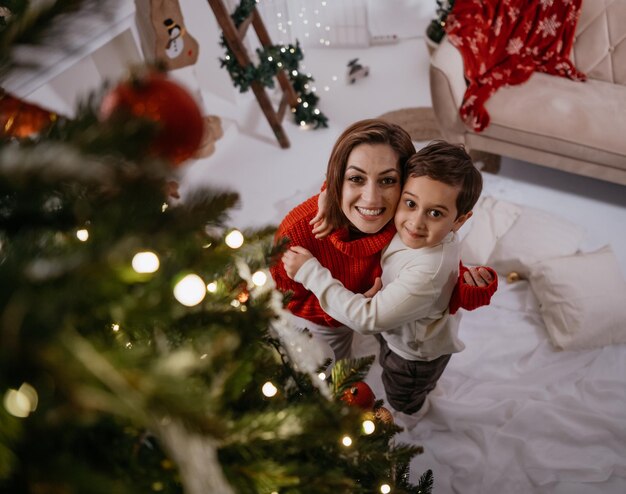 Vreugdevolle alleenstaande moeder en haar kleine zoon omhelzen en kijken camera met aangename glimlach op gezellige h