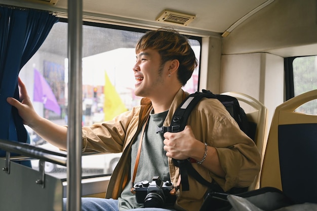 Vreugdevolle Aziatische man zit en kijkt door het raam van de bus Reizen en transport concept