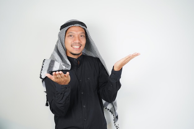 Vreugdevolle Aziatische moslimman met een Arabische turban en een sorban die met zijn vinger naar de lege ruimte op een geïsoleerde