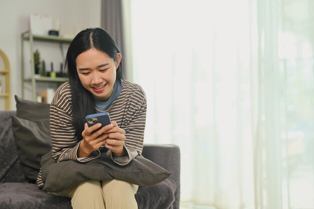 Foto vreugdevolle jonge vrouw die nieuws en berichten op het sociale netwerk op haar mobiele telefoon controleert