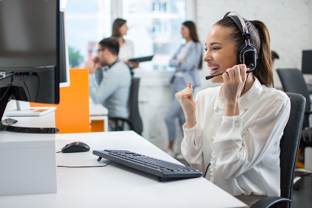 Vreugdevolle jonge vrouwelijke technische ondersteuningsagent die de vuist omhoog houdt en het succesvolle einde van het werk met de klant in het callcenter viert Concept van goed gedaan werk in het klantensupportcentrum