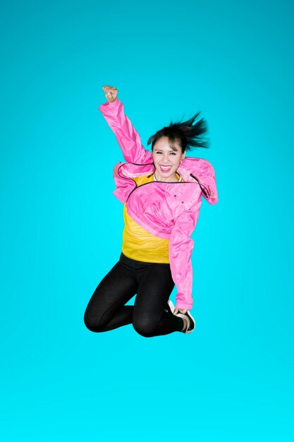 Foto vreugdevolle moderne danseres springt met sweatshirt in de studio op blauwe achtergrond