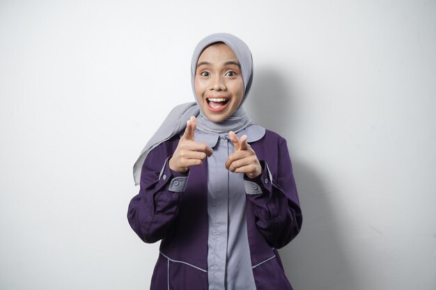 Vreugdevolle mooie Aziatische vrouw in casual shirt en hijab wijst naar een lege ruimte geïsoleerd door een witte achtergrond