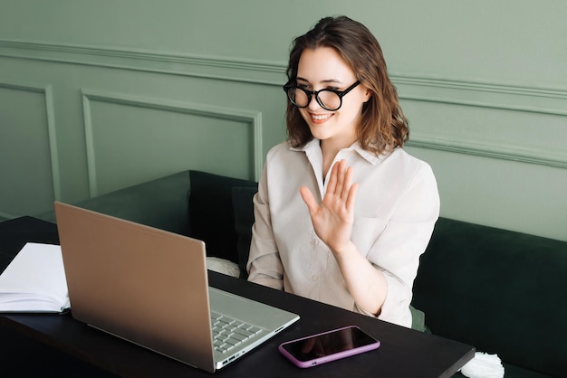 Vreugdevolle videochat Jonge vrouw met een bril die groeten deelt Expressieve online interactie Joyf