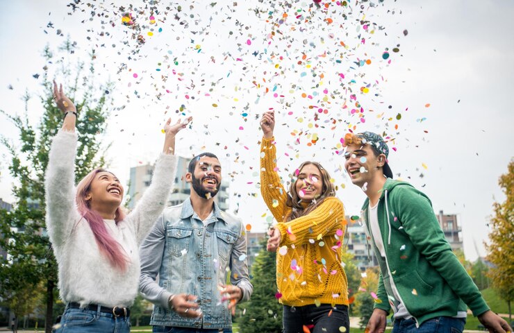 Foto vreugdevolle vrienden die confetti gooien terwijl ze in het park staan.