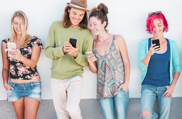 Vreugdevolle vrienden die tegen de muur staan en telefoons gebruiken