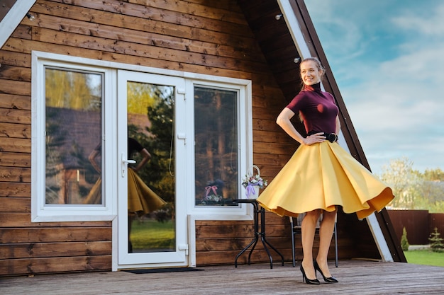 Vreugdevolle vrouw in lange zwaaiende rok en paarse trui die op het terras van een aframe hut danst