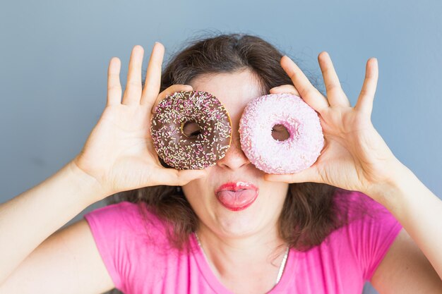 Vreugdevolle vrouw met donuts tegen de muur.