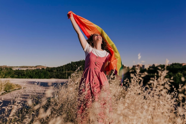 Foto vreugdevolle vrouw met regenboogvlag terwijl ze op het veld staat