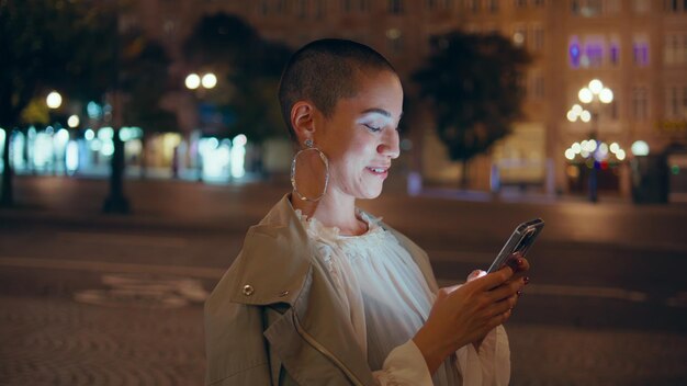 Foto vreugdevolle vrouw schrijft een bericht op een smartphone op een donkere straat. close-up meisje sms't.