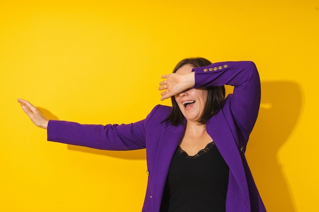 Vreugdevolle vrouw van middelbare leeftijd met een paarse blazer die tegen een gele achtergrond danst