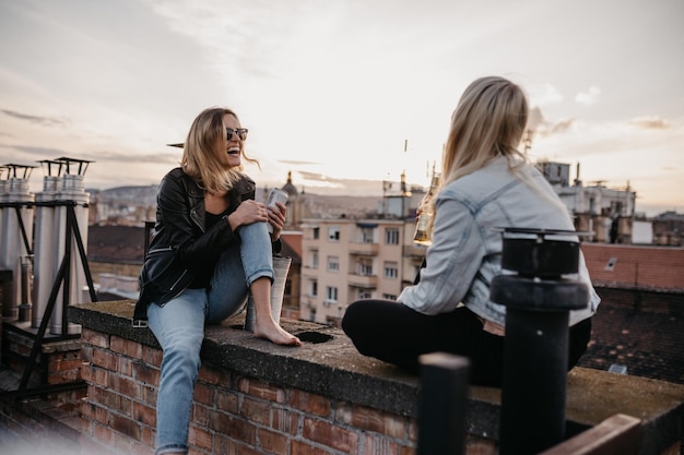 Vreugdevolle vrouwen praten terwijl ze op een terras tegen de lucht zitten.