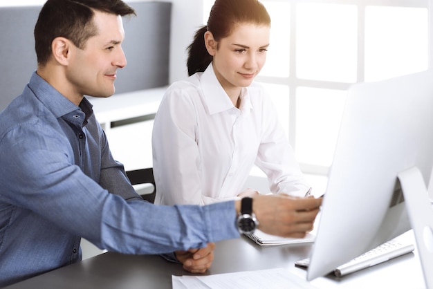 Vriendelijk lachende zakenman en vrouw die werkt met de computer in moderne kantoren. Headshot op vergadering of werkplek. Teamwork, partnerschap en bedrijfsconcept.