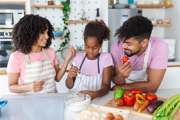 Vriendelijke Afrikaanse ouders die hun schattige dochter leren hoe ze gezond voedsel kunnen koken in de vrije ruimte