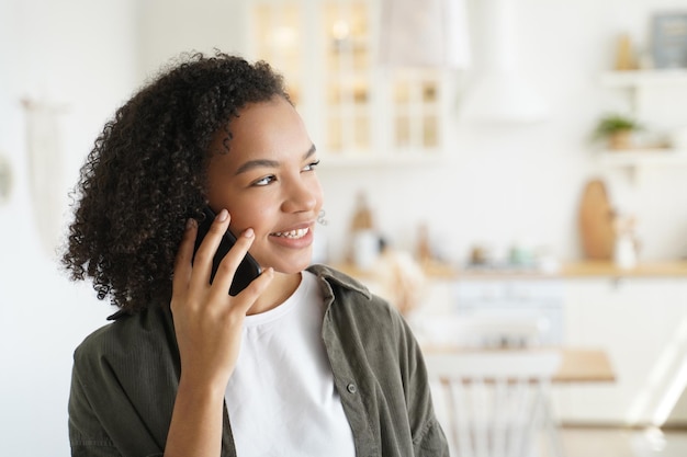 Vriendelijke Afro-Amerikaanse tienermeisje praten op smartphone maakt mobiel telefoontje vanuit huis