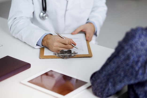 Vriendelijke arts met rode baard en geduldige vrouw bespreken het huidige gezondheidsonderzoek terwijl ze in een zonnige kliniek zitten. Geneeskunde concept.