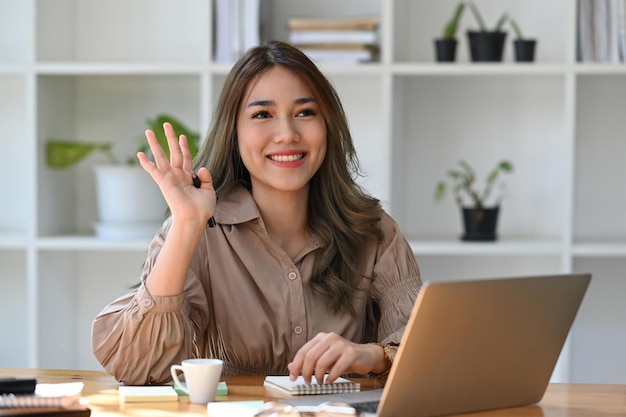 Vriendelijke Aziatische vrouw kantoormedewerker groet collega's tijdens het werken met computer laptop