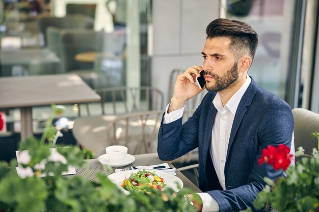 Vriendelijke brunette man die aan tafel zit en buiten op het terras gaat eten