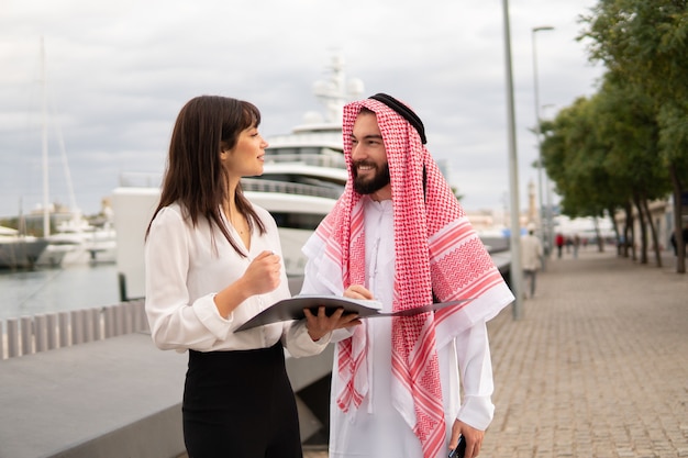 Vriendelijke europese zakenvrouw en glimlachende arabische man bespreken contractvoorwaarden tijdens een ontmoeting in de haven