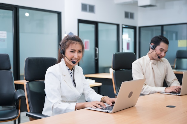 Vriendelijke exploitant Aziatische vrouw agent met hoofdtelefoon werken met laptop op overleg van de klant op kantoor met collega op de werkplek