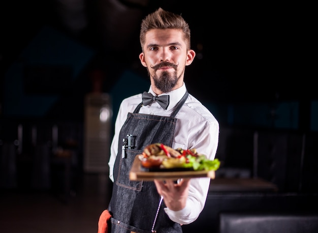 Vriendelijke flunky houdt behulpzaam gekookt gerecht vast in het restaurant.