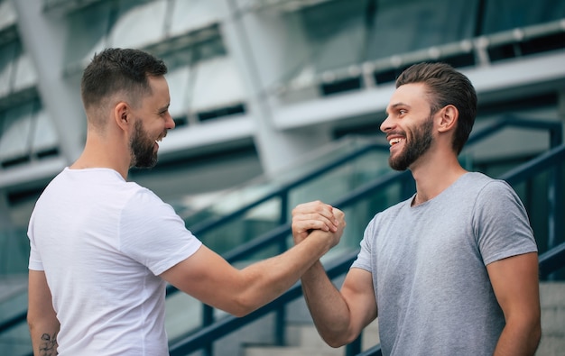 Vriendelijke handdruk voor mannen. Twee jonge, bebaarde knappe vrienden in casual t-shirts poseren samen