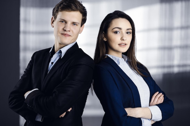 Vriendelijke jonge collega's staan als een team met gekruiste armen in een modern kantoor. Portret van succesvolle zakenmensen op het werk.